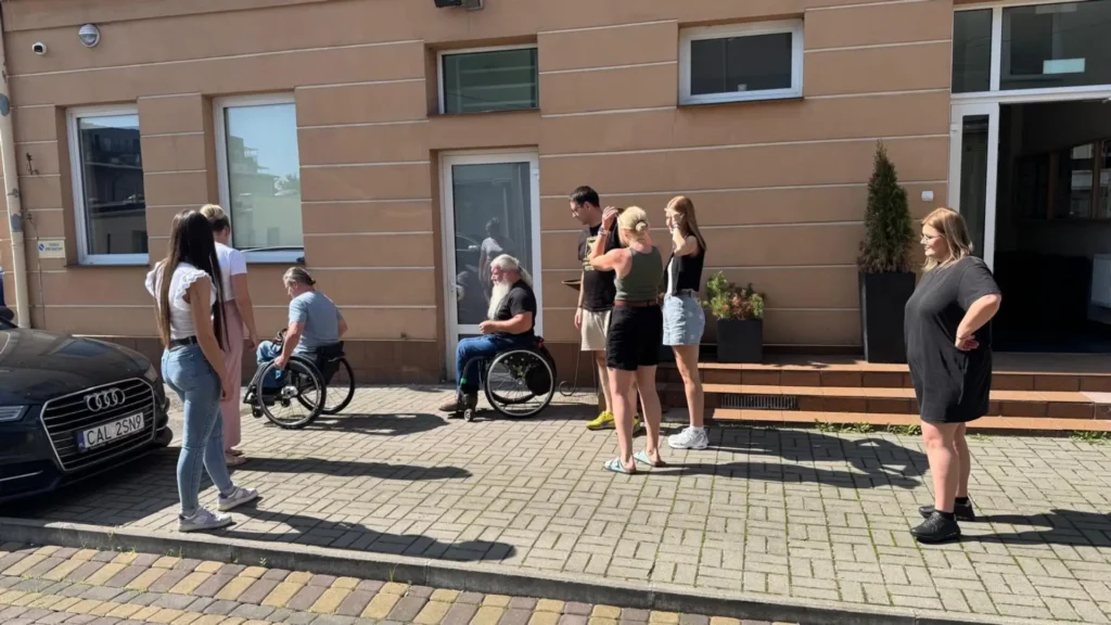 Grupa uczestników szkolenia z dostępności przed budynkiem Instytutu Pielęgniarstwa, w tym osoby z niepełnosprawnościami.