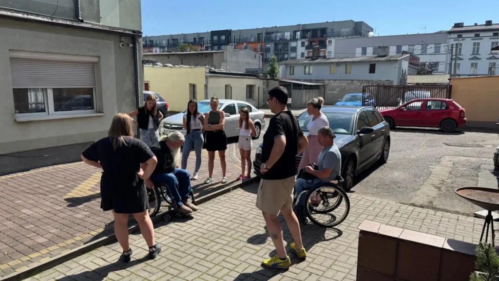 Uczestnicy szkolenia z dostępności przed budynkiem Instytutu Pielęgniarstwa Wyższej Szkoły Nauk o Zdrowiu w Bydgoszczy, w tym osoby z niepełnosprawnościami i studenci.